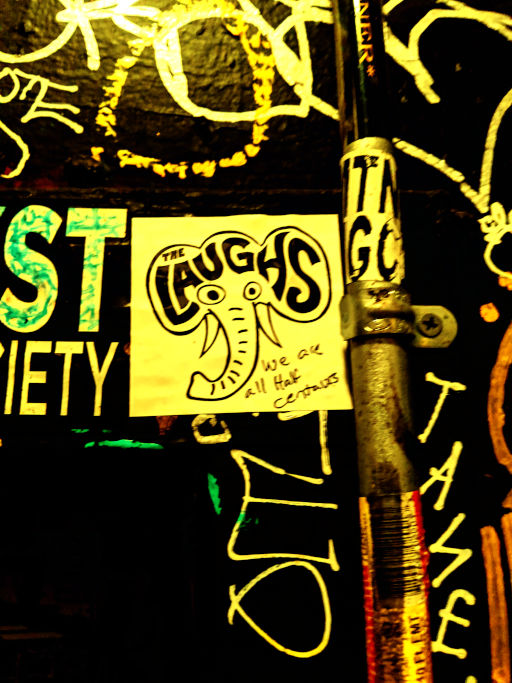Hand-drawn Laughs elephant poster taped to a graffiti-covered pole at night