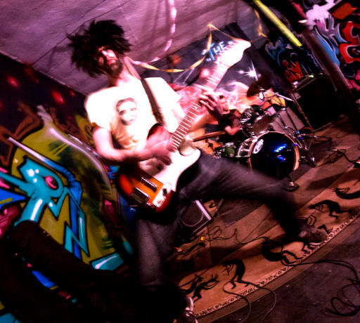 Guitarist playing beneath pink lights in front of a graffiti wall