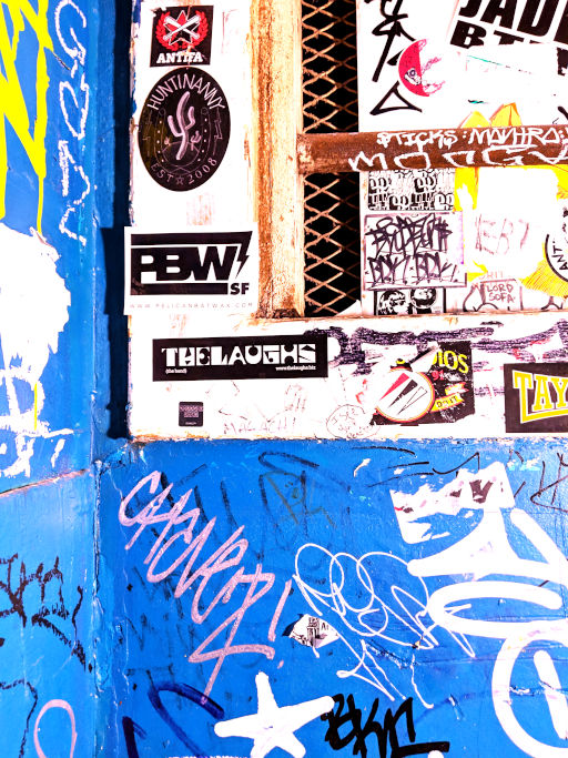 Close-up of a graffiti-covered wall and gate with a Laughs sticker