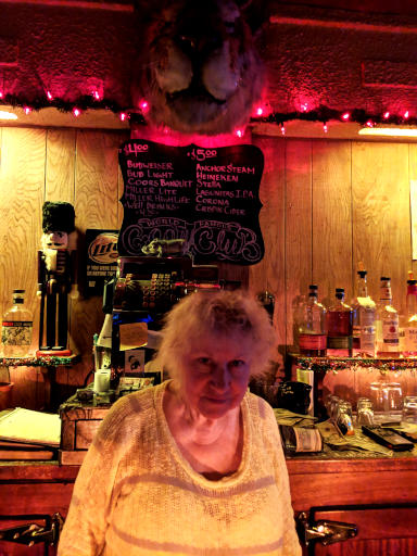 Older patron sitting at a bar beneath its chalkboard menu